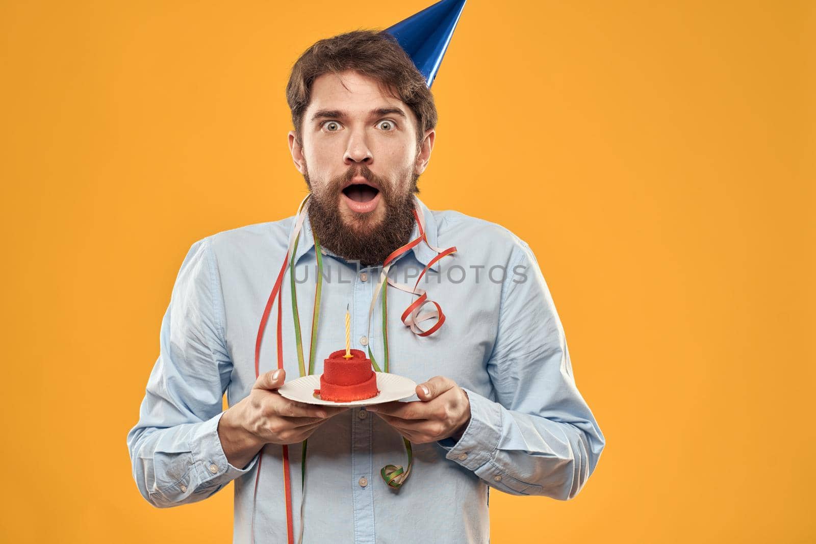 Cheerful man with a cake on a yellow background birthday holidays cap on his head. High quality photo