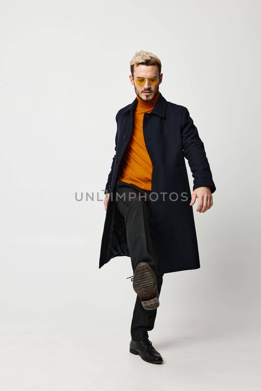 modern man in a dark coat and full-length trousers on a light background and glasses on his face. High quality photo