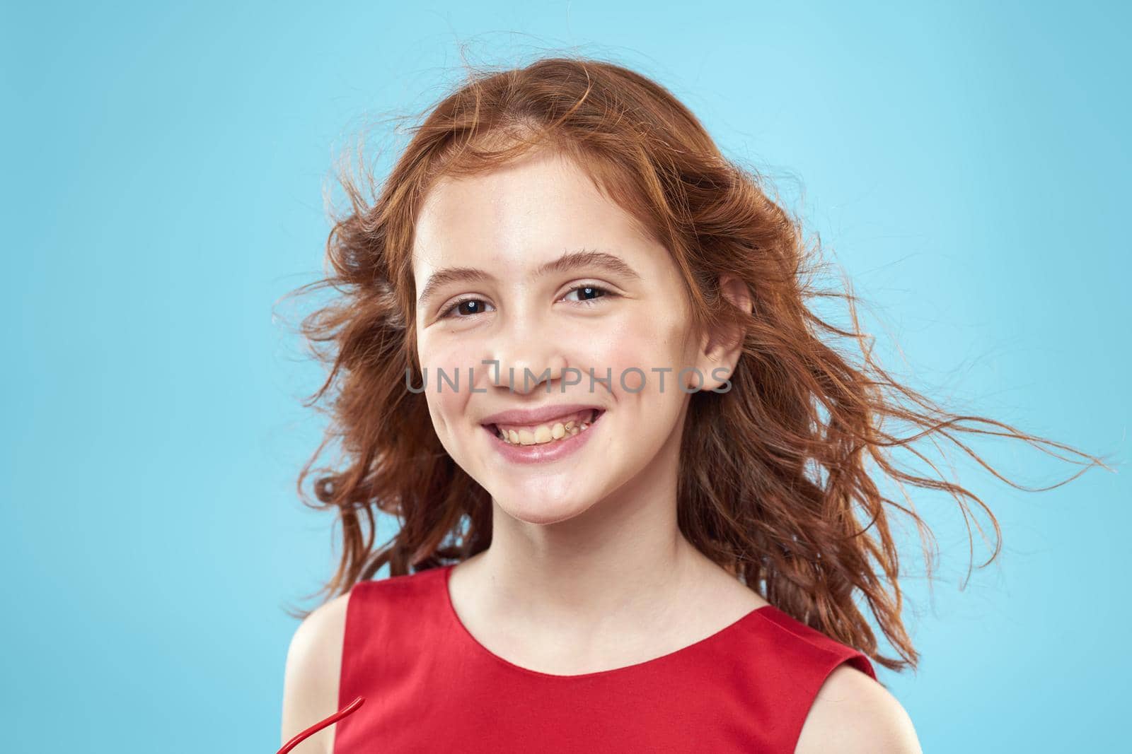 little girl with curly hair with a crown on her head red dress Smile blue background. High quality photo