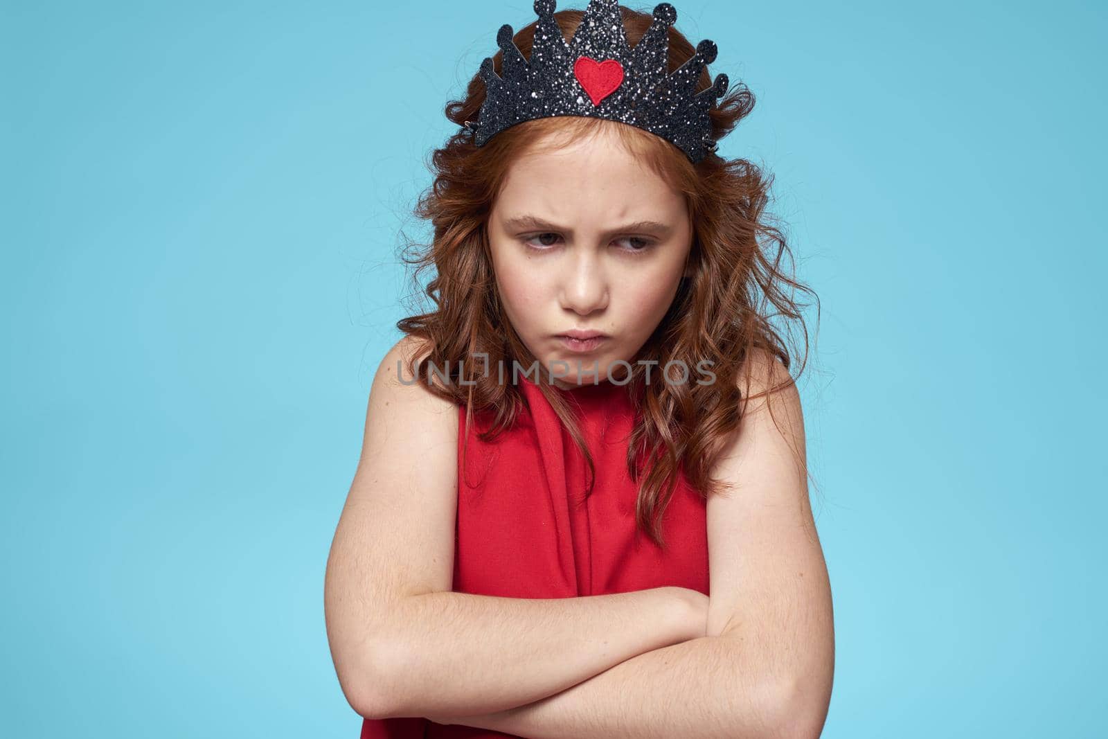 Girl with curly hair with a crown on her head red dress lifestyle blue background. High quality photo