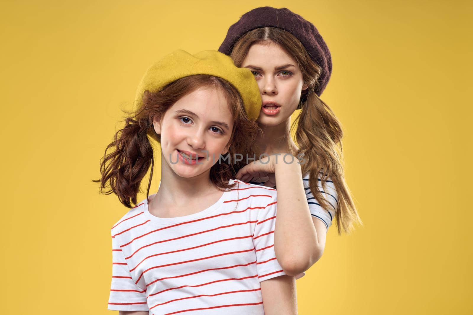 Cheerful sisters in hats striped T-shirts joy lifestyle yellow background family. High quality photo