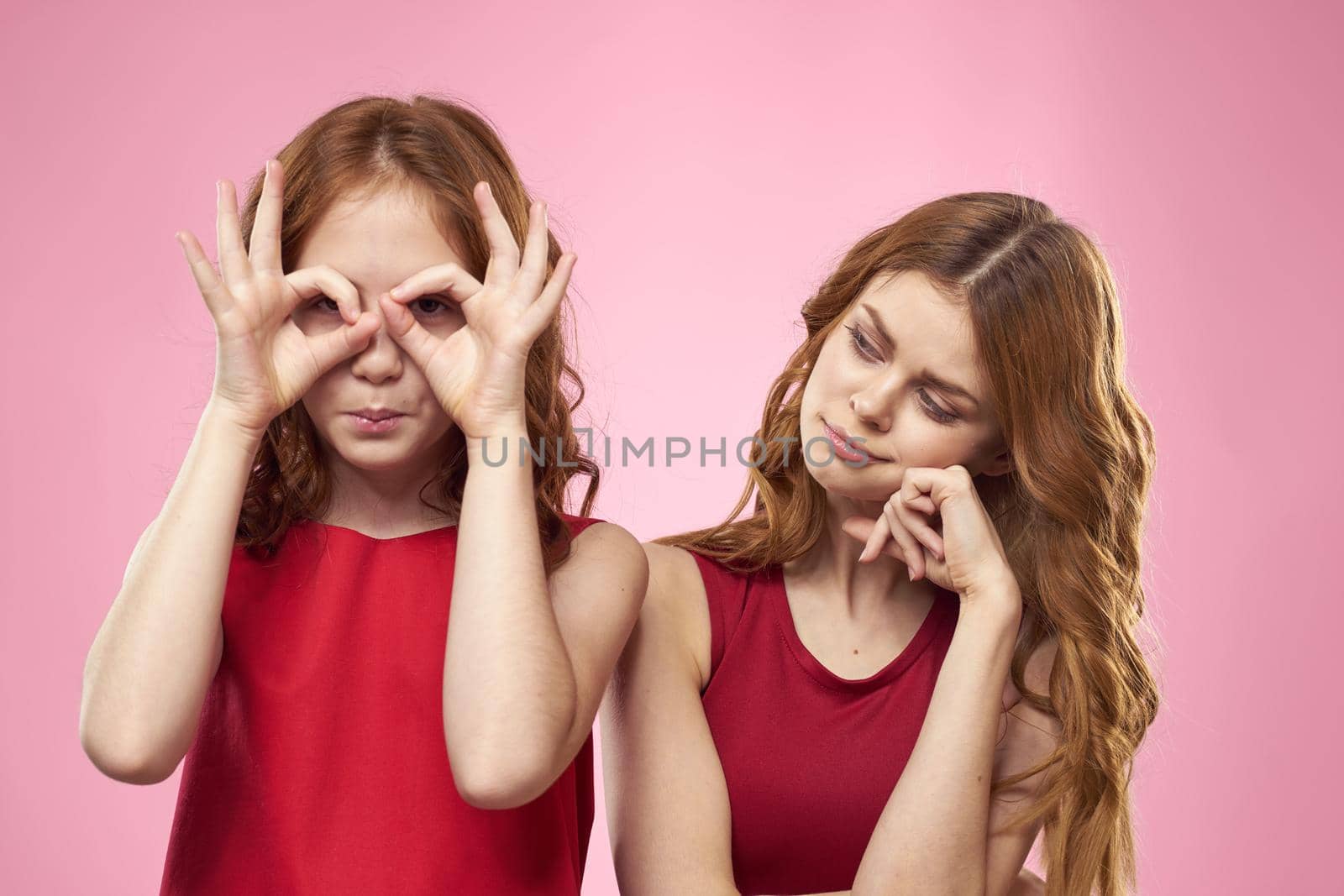 Mom and daughter in red dresses hugs fun grimace childhood joy pink background. High quality photo