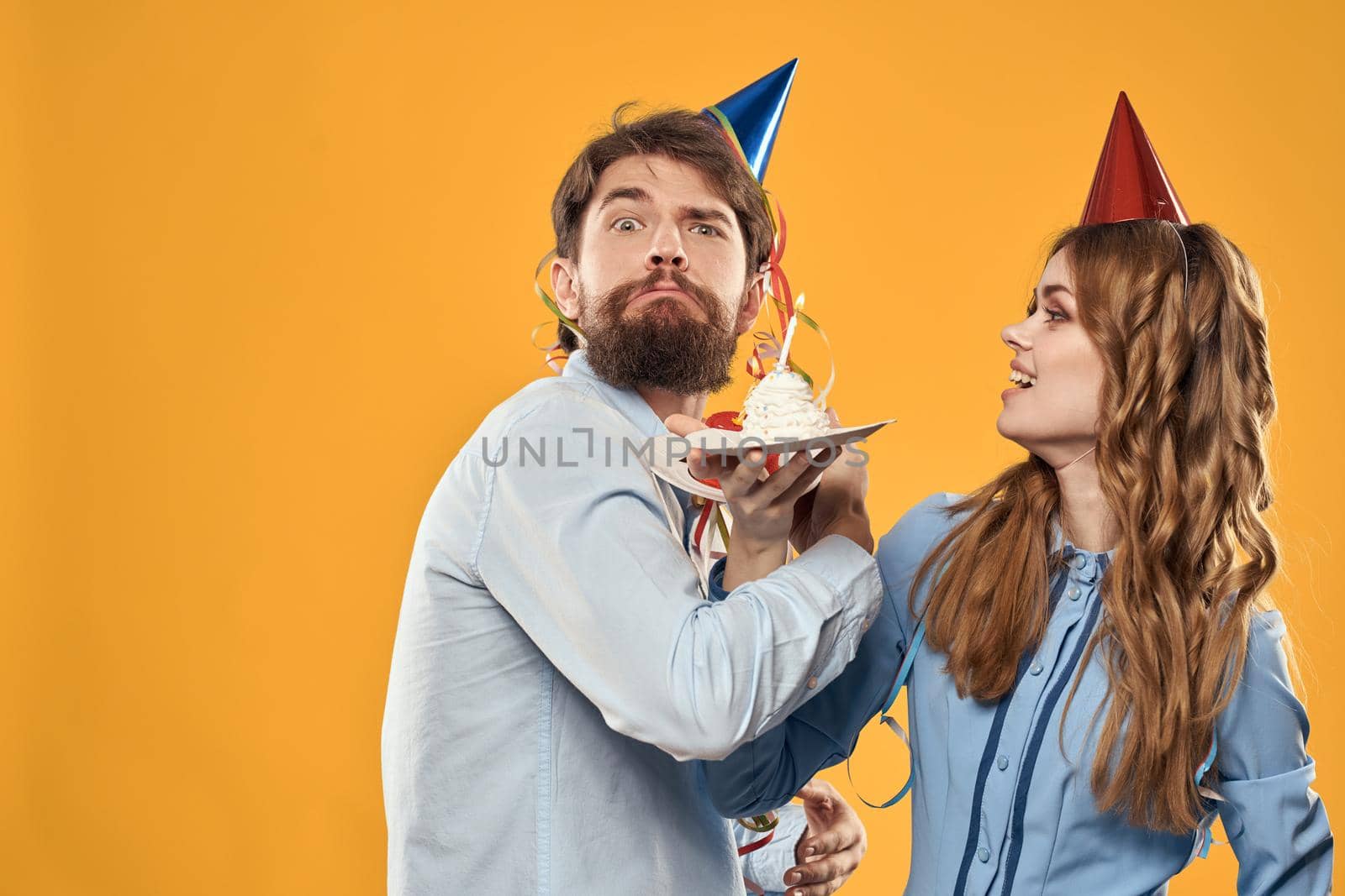 Man and woman at a party in caps and with tinsel cake fun yellow background. High quality photo