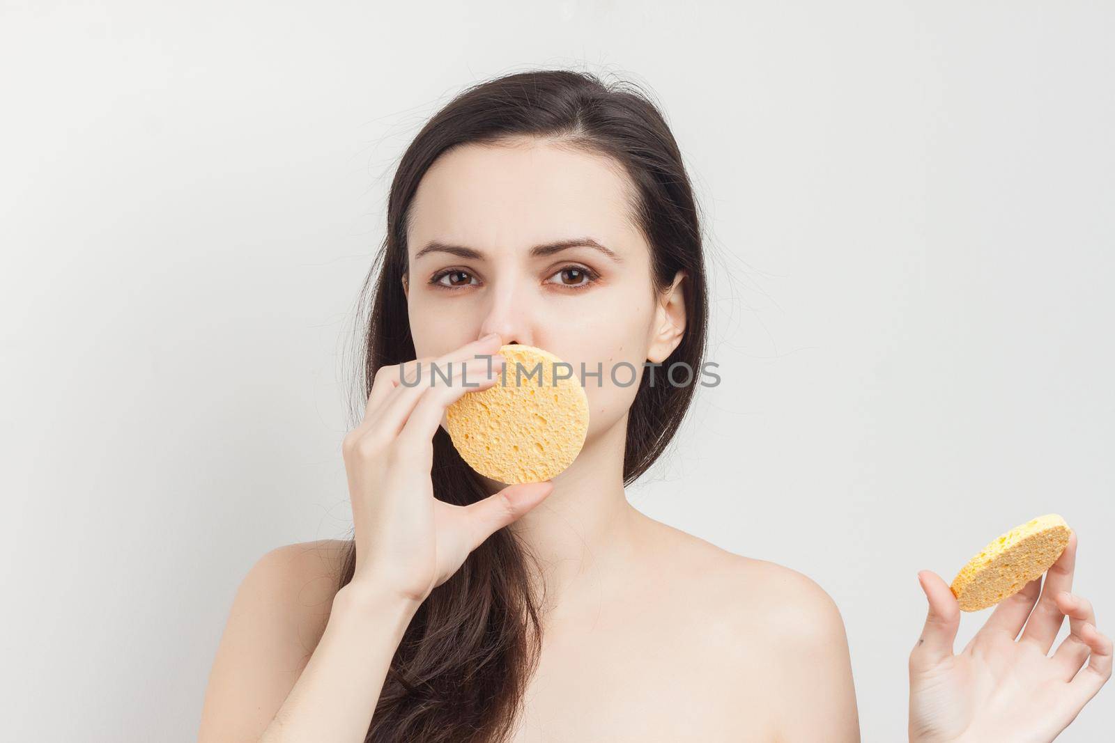 brunette with flowing hair naked shoulders sponge near face. High quality photo