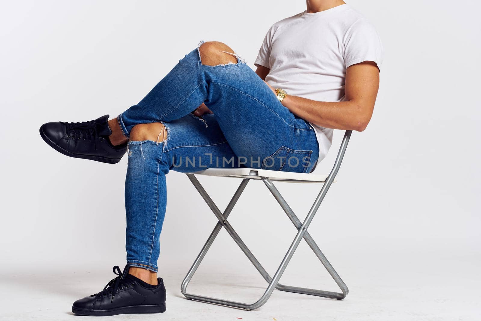 a man in jeans and a t-shirt sits on a chair on a light background side view. High quality photo
