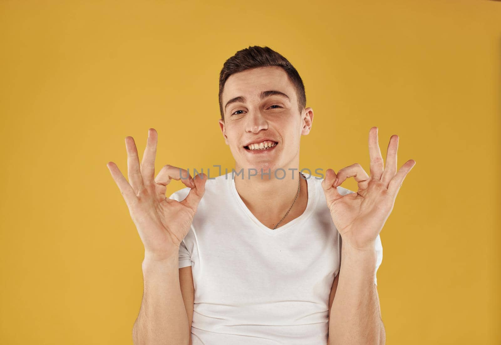 happy brunette man on yellow background shows positive hand gesture. High quality photo