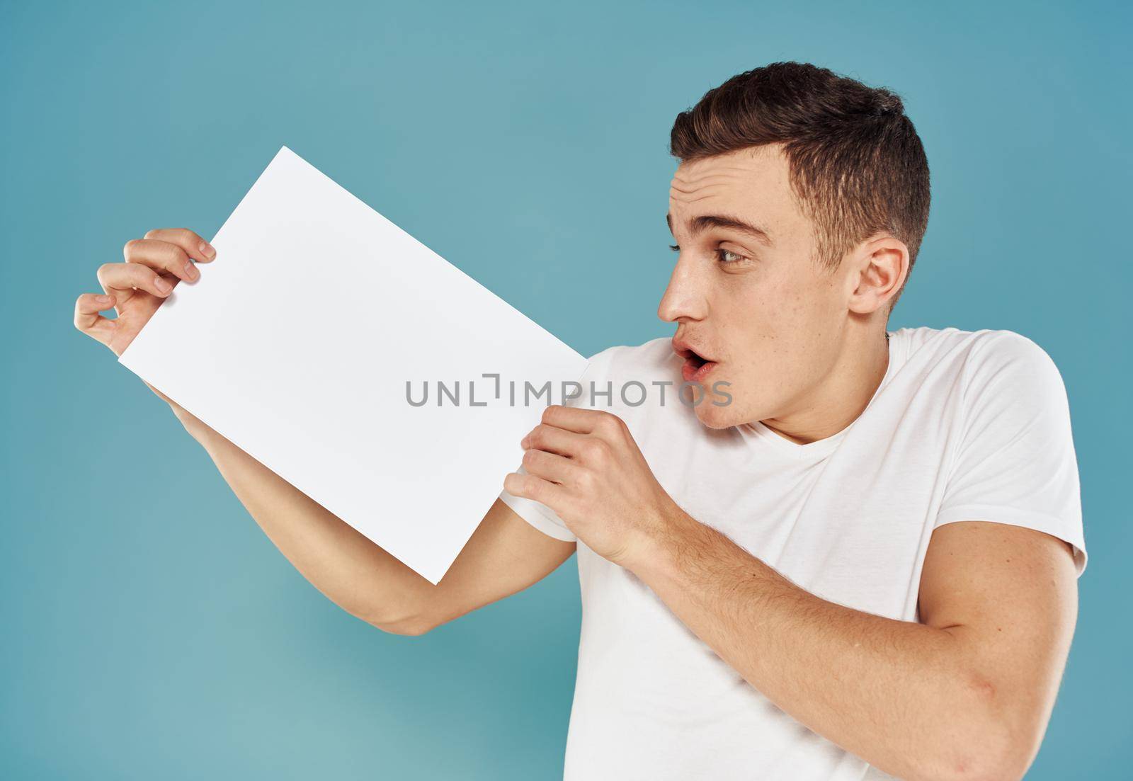 Happy guy shows a flyer in his hand on a blue background advertising mockup. High quality photo