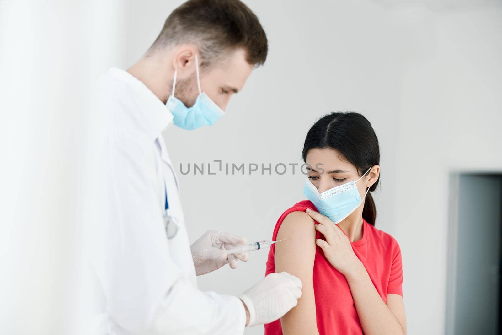 male doctor in a medical mask injections in the shoulder of a woman health coronavirus by SHOTPRIME