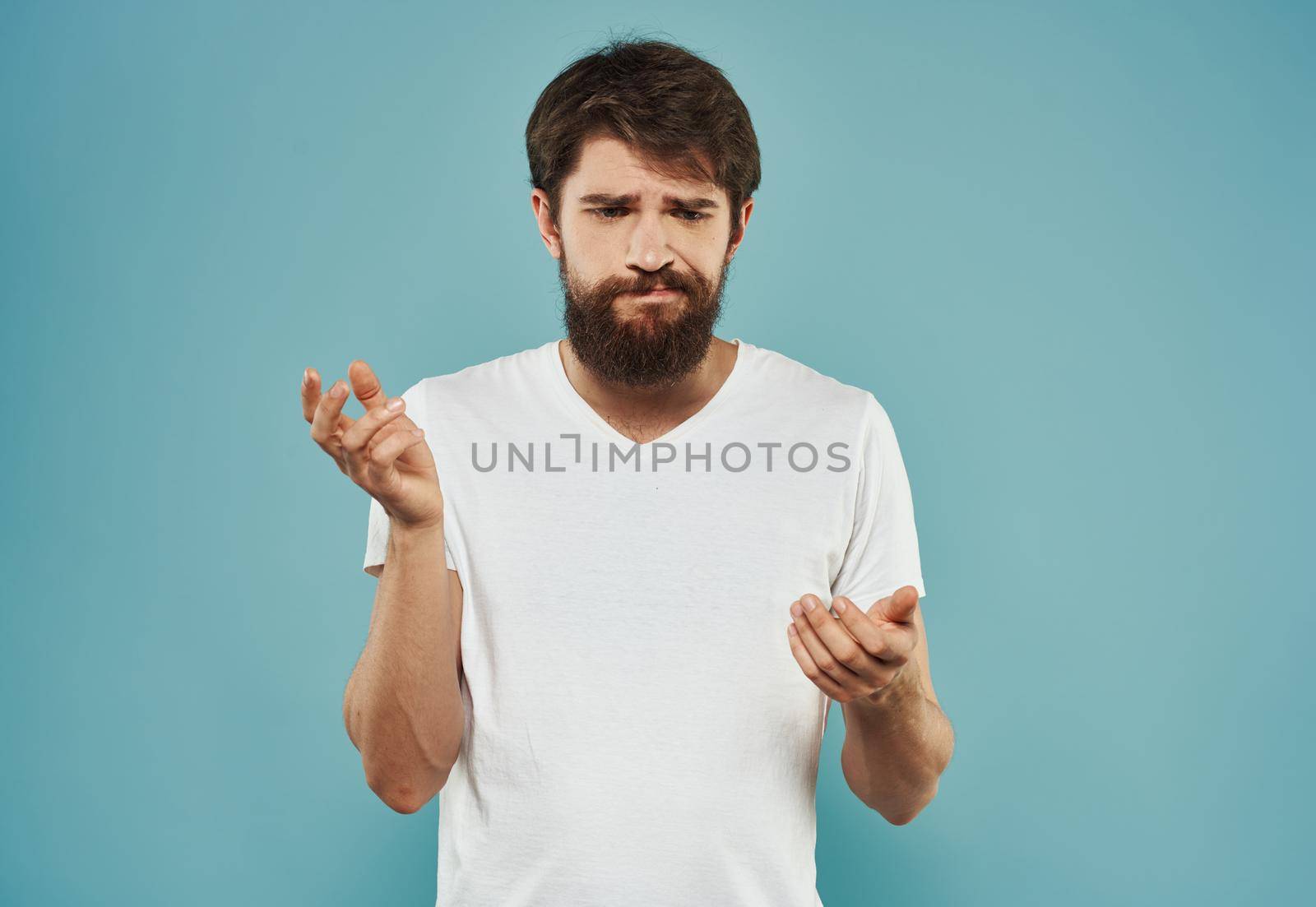 A brunette guy with a thick beard on a blue background gestures with his hands cropped view. High quality photo