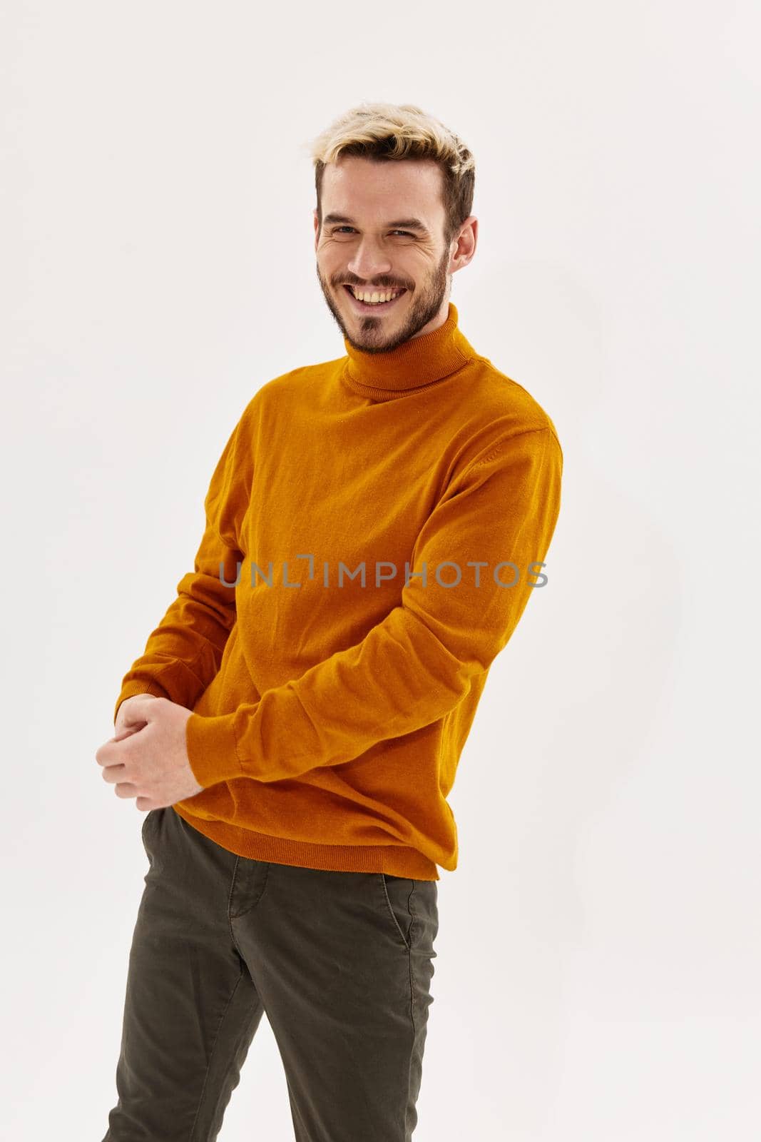 happy blond guy in an orange sweater and trousers laughs on a light background by SHOTPRIME