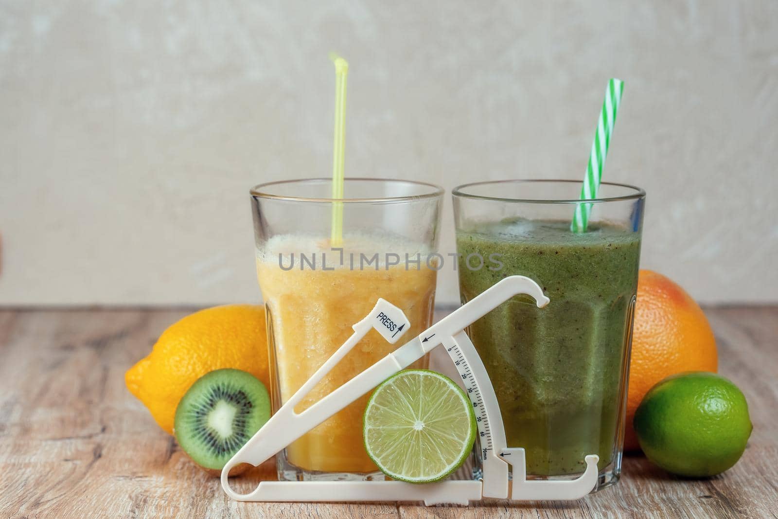 Tall glasses of kiwi and spinach smoothies in a row surrounded by fruits and caliper on a wooden table. The concept of losing weight and proper nutrition.