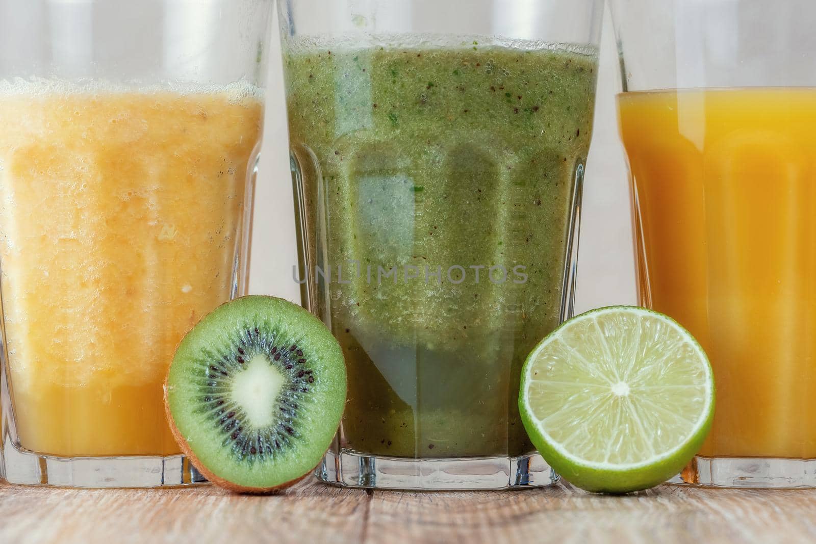Three tall glass with kiwi and spinach smoothies in a row surrounded by fruits by galinasharapova