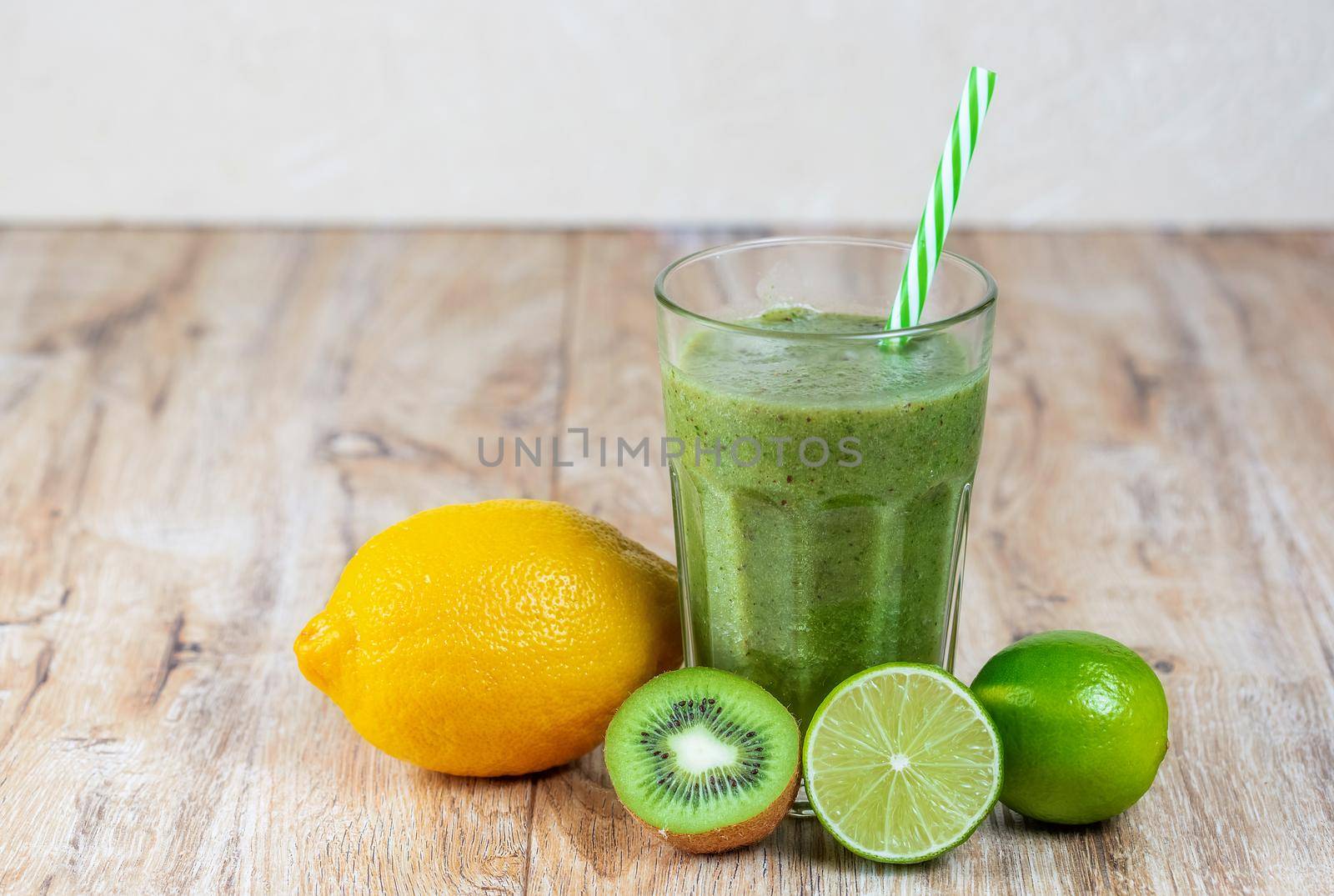 Tall glass with kiwi and spinach smoothie surrounded by fruits on a wooden table. The concept of losing weight and proper nutrition.