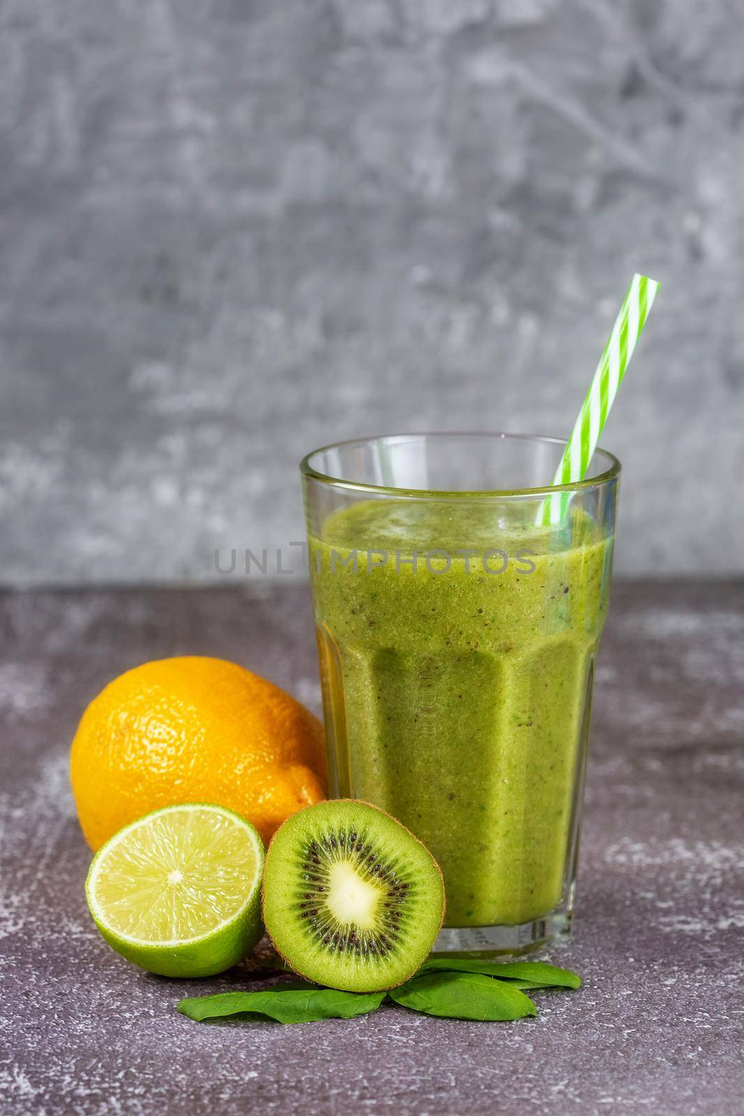 Fresh healthy smoothie drink in a tall glass glass with a straw surrounded by fruits on a gray concrete background. The concept of proper nutrition, weight loss, detoxification of the body.