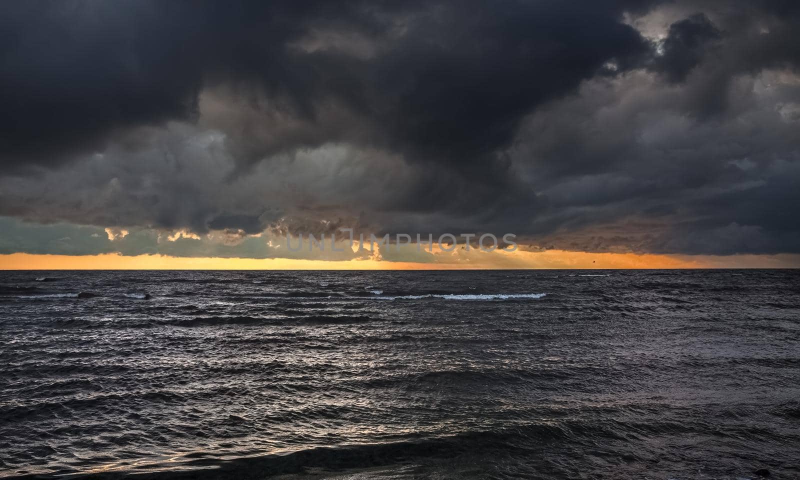 Amazing dramatic landscape. Dramatic dark clouds during sunset at sea. Dark sea water and heavy beautiful grey clouds.
