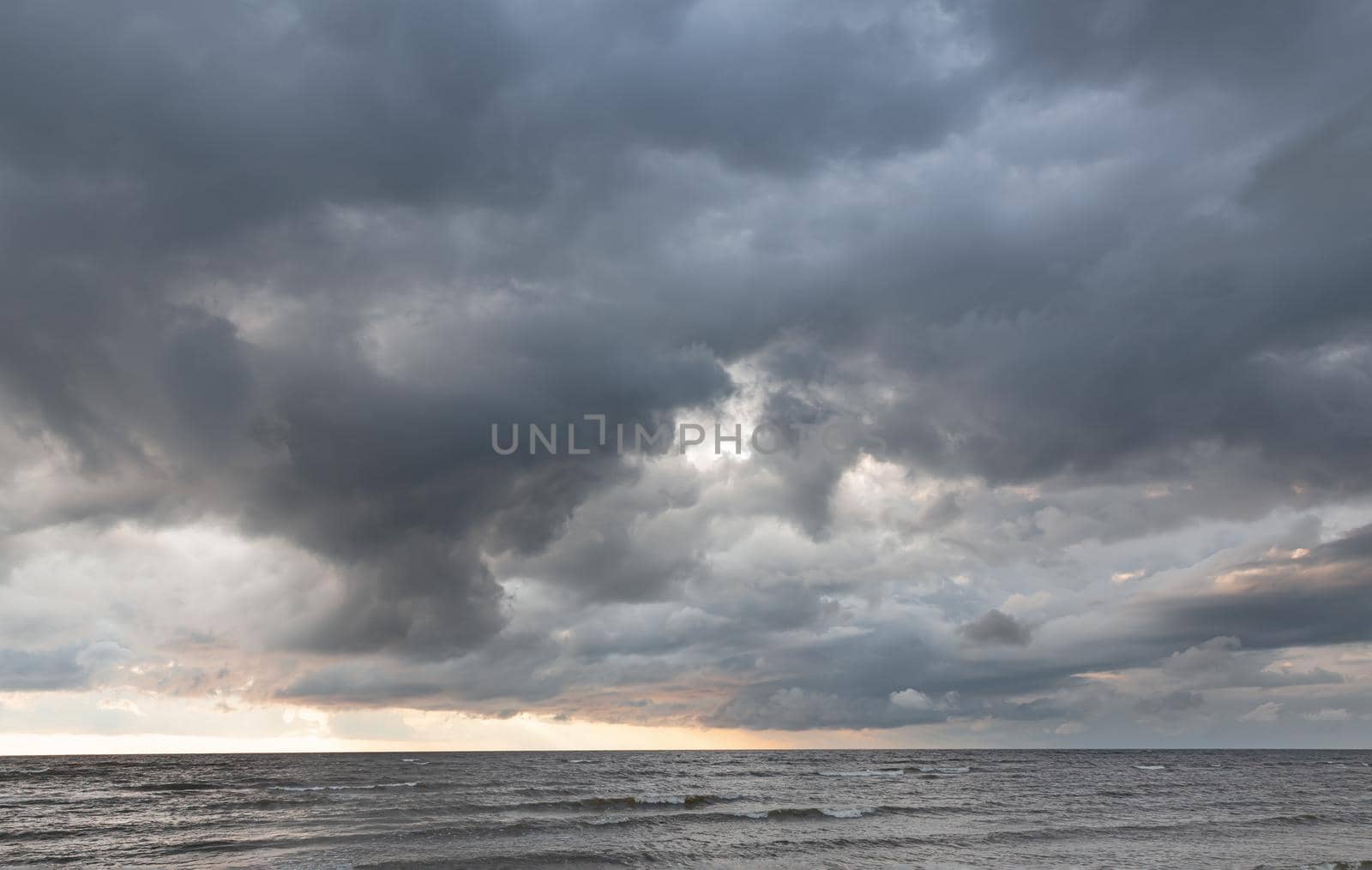 Amazing dramatic landscape. Dramatic dark clouds during sunset at sea. Dark sea water and heavy beautiful grey clouds.