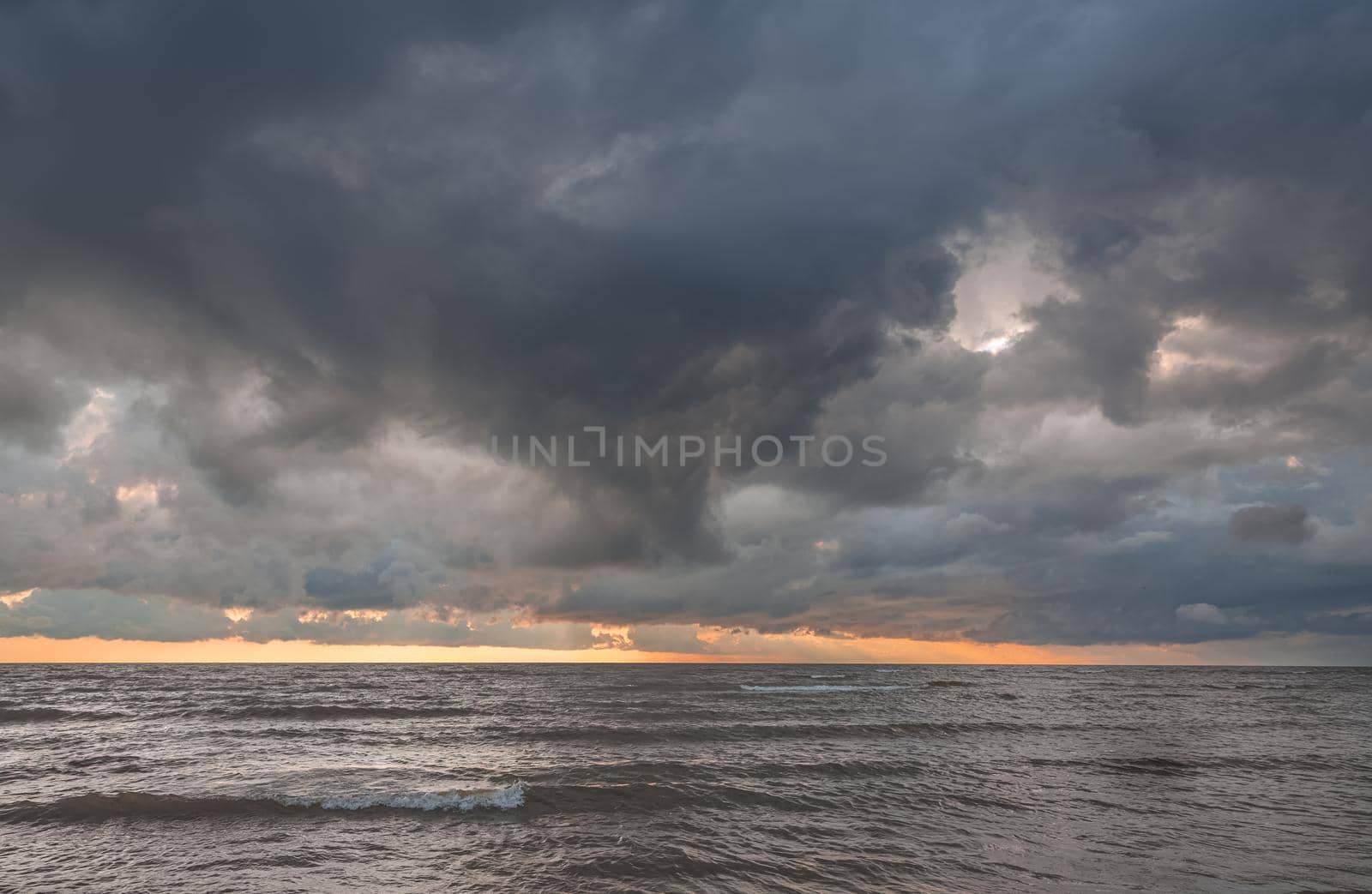 Amazing dramatic landscape. Dramatic dark clouds during sunset at sea. Dark sea water and heavy beautiful grey clouds.