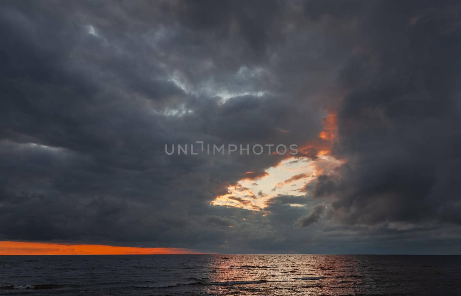 Amazing dramatic landscape. Dramatic dark clouds during sunset at sea. Dark sea water and heavy beautiful grey clouds.