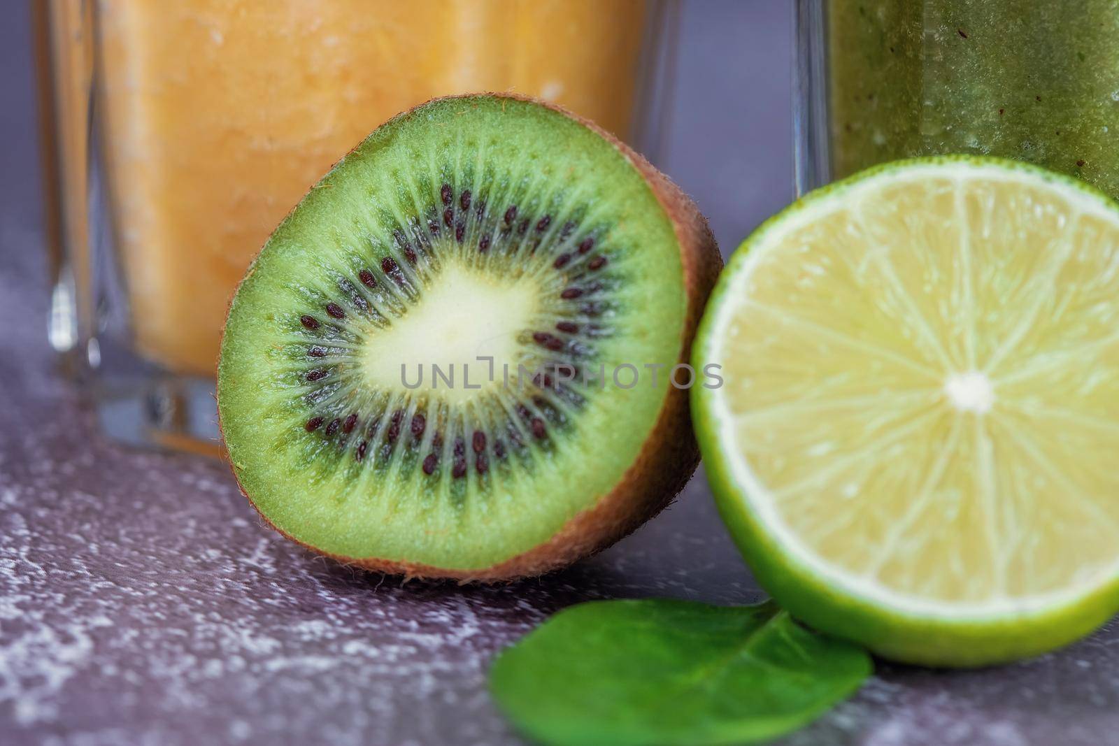 A close-up of lime and kiwi fruit halves in front of glasses of orange juice and spinach smoothie. The concept of losing weight and proper nutrition.
