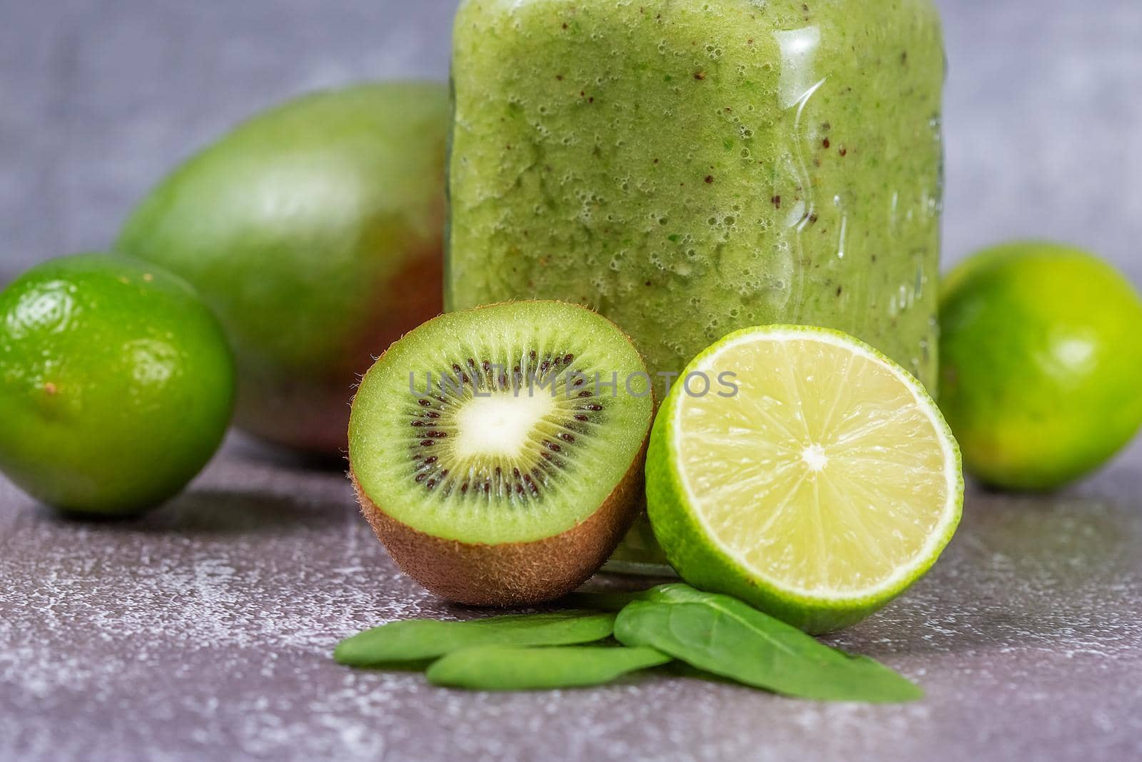 Close-up of fresh kiwi and lime fruit halves against a smoothie mug on a gray concrete backdrop. The concept of a healthy lifestyle and proper nutrition. Good for your health. Vitamin drink.