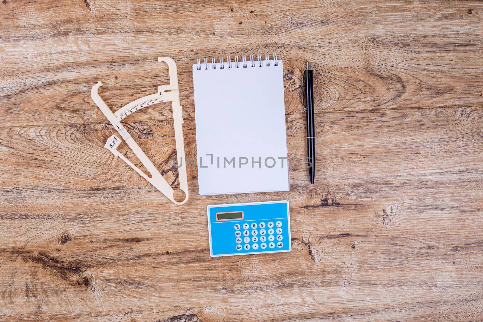 Blank sheet of notepad pen calculator and caliper on wooden table layout. by galinasharapova