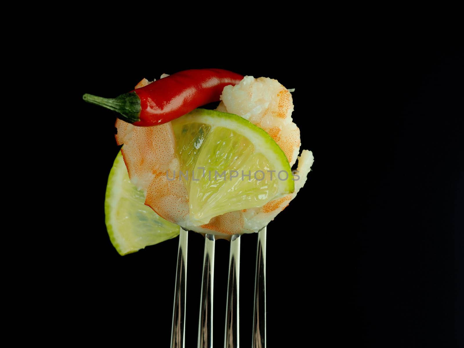 The kings shrimp on a fork with lime, on a black background. High quality photo