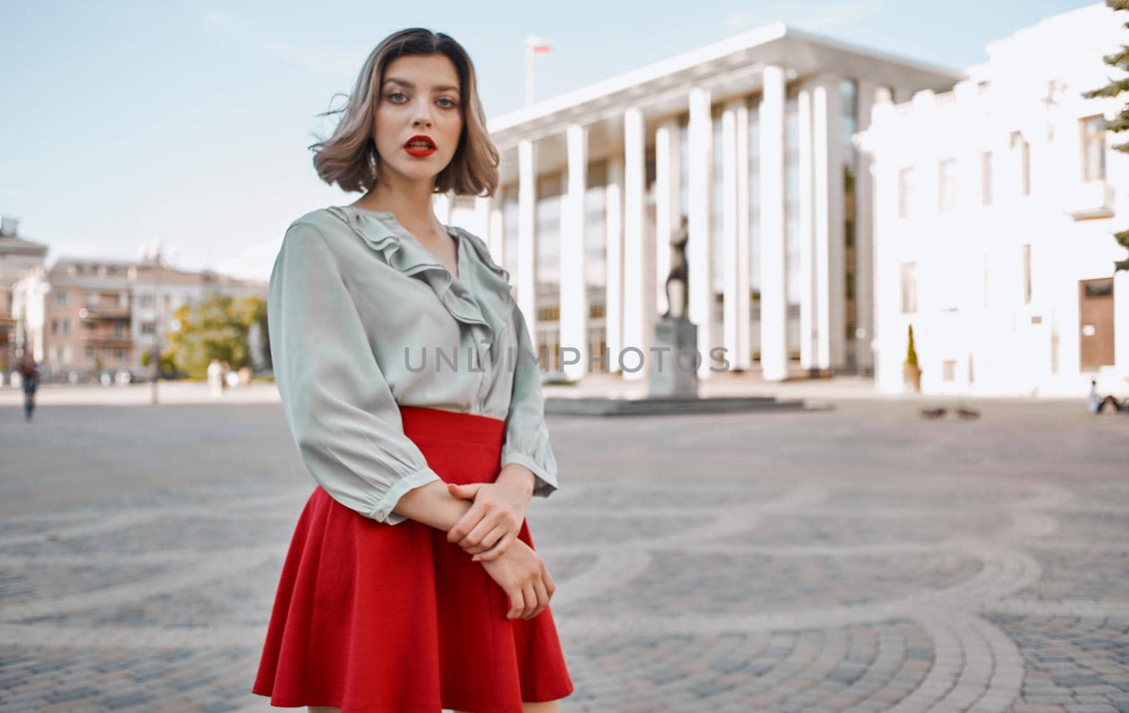 woman with bright makeup in a shirt and in a red skirt are walking on the street in summer near the building. High quality photo
