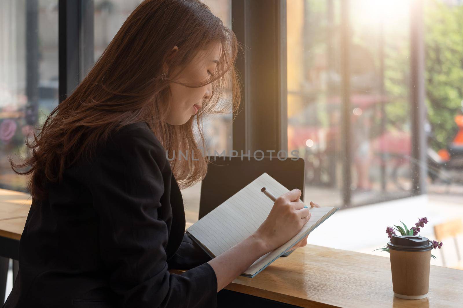 Business woman taking notes in a book with laptop on table by nateemee