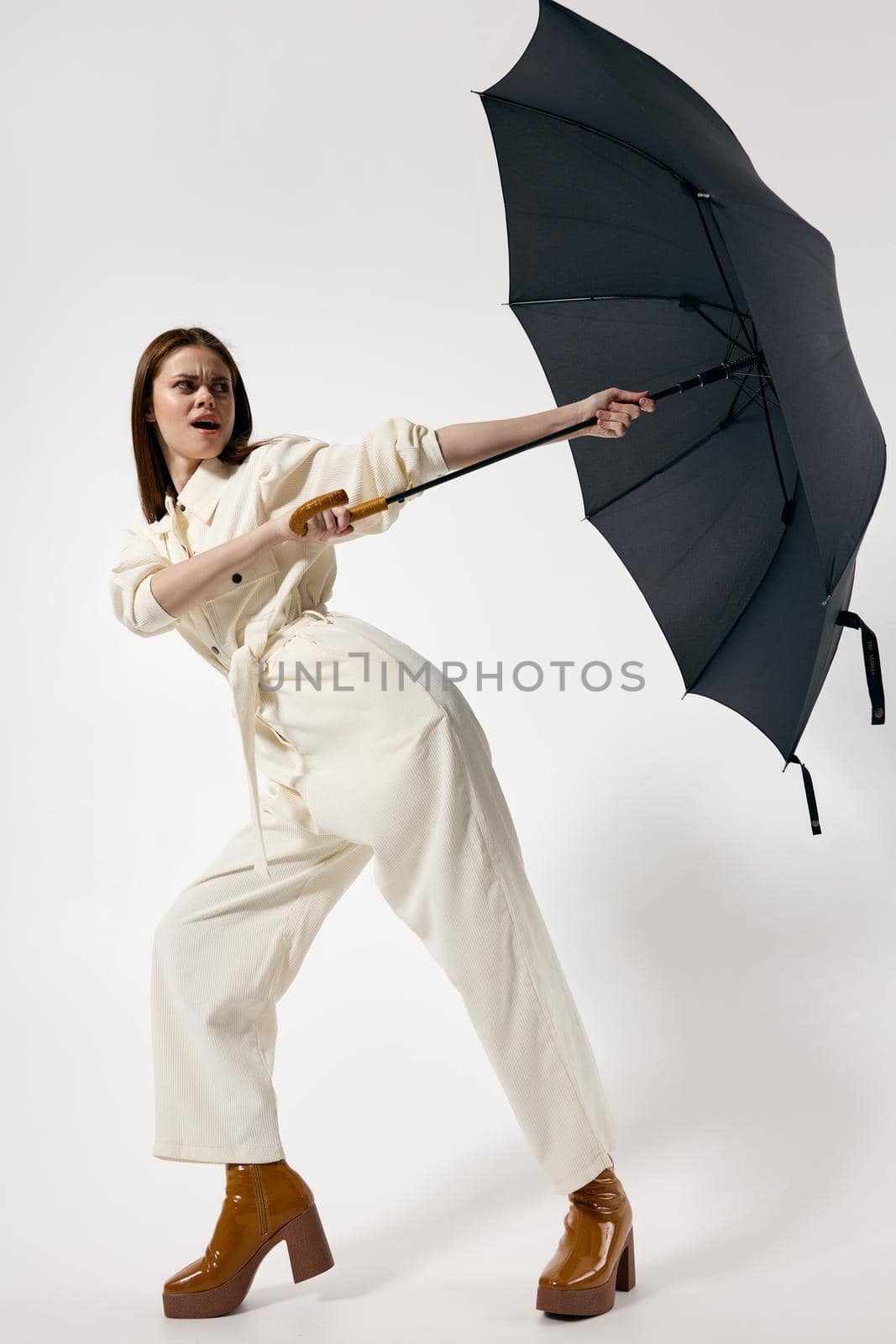 Woman in white suit holding an umbrella from the wind modern style fashion studio. High quality photo