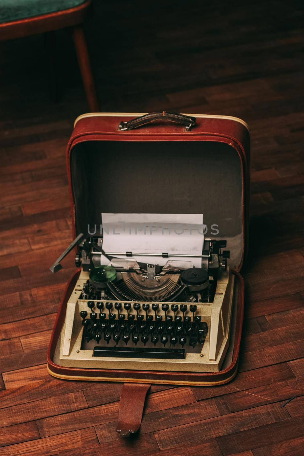 vintage typewriter with white paper stands on the floor indoors by SHOTPRIME