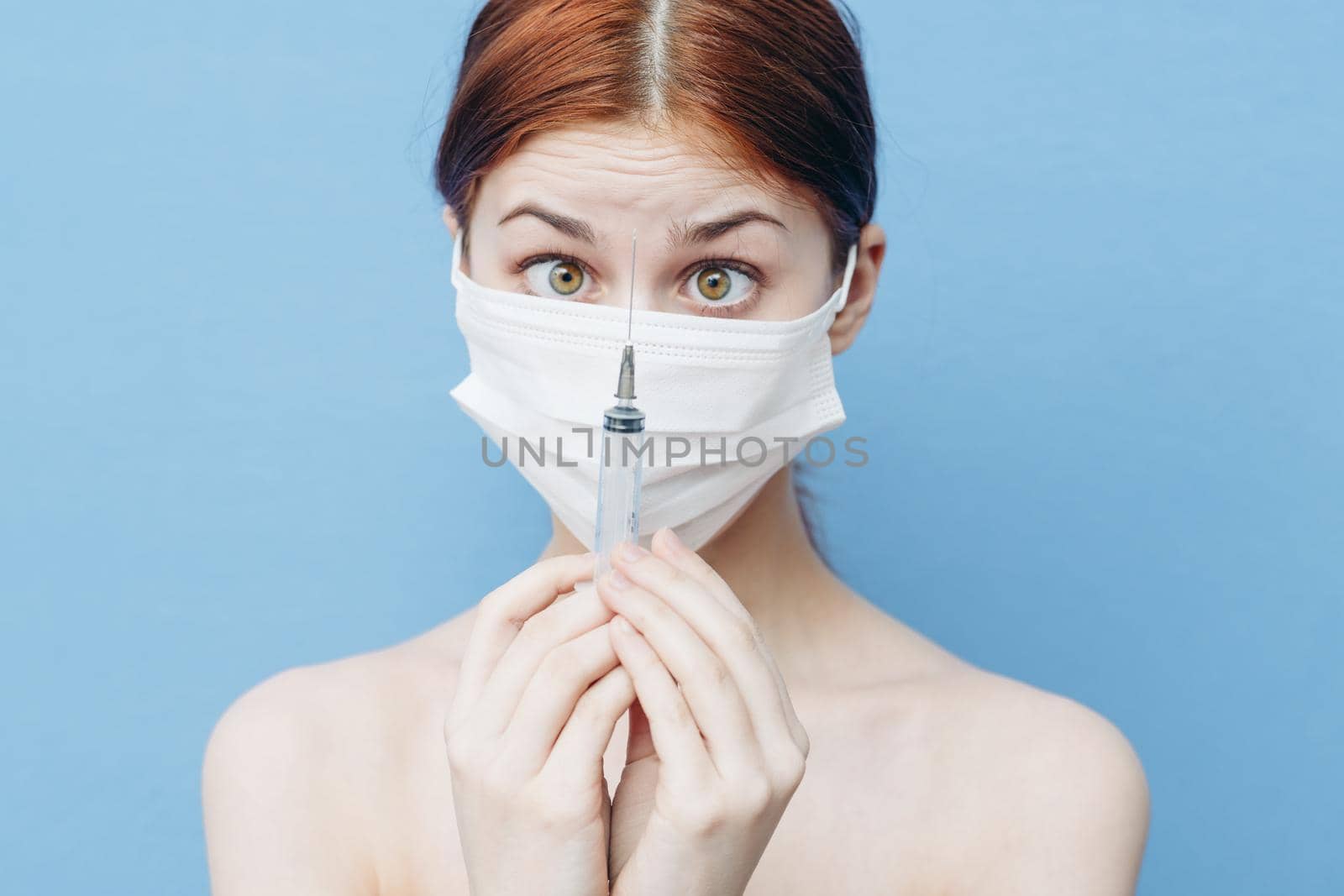woman with syringe in hand and medical mask injection blue background. High quality photo