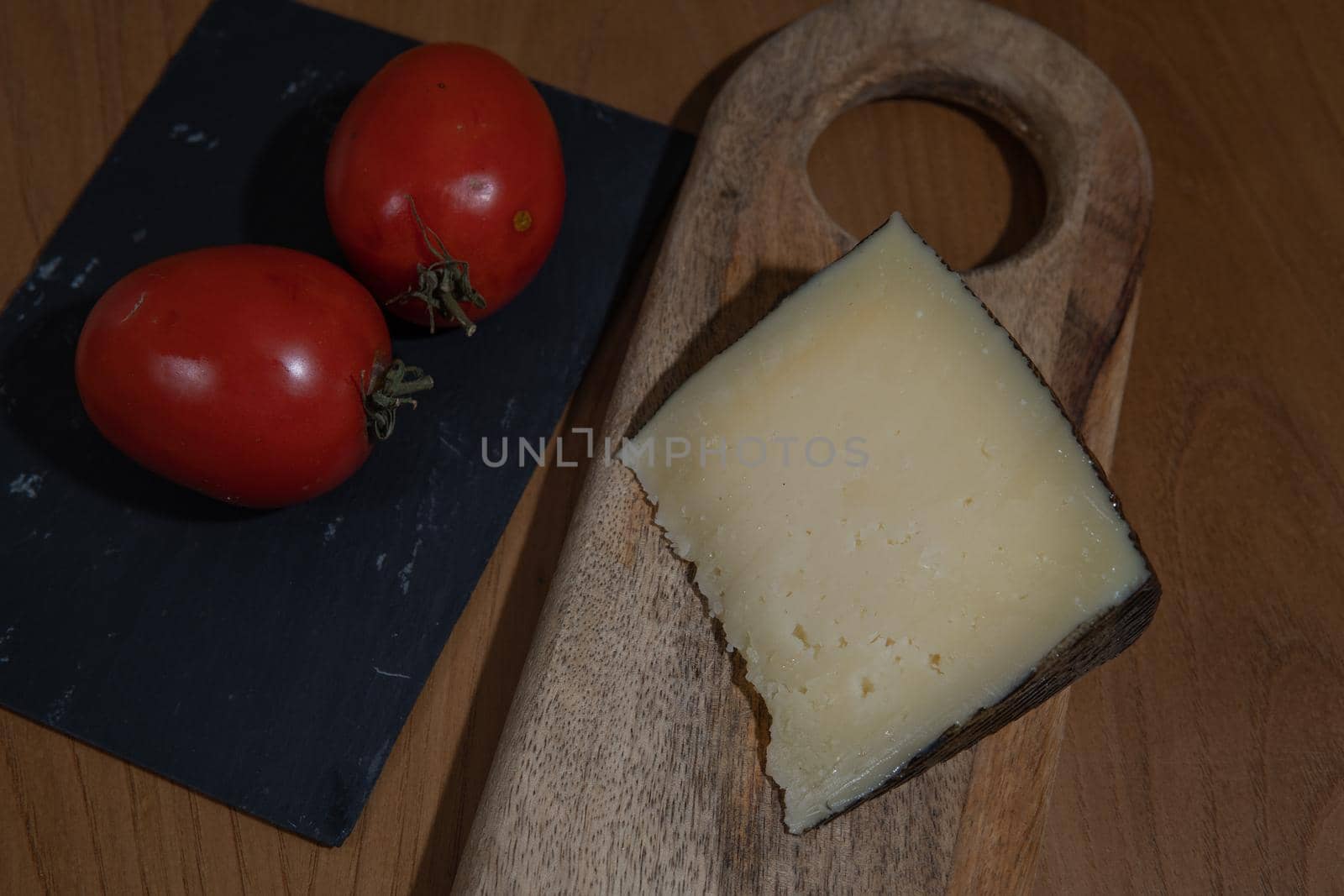 Cheese wedge with tomato on wooden plank