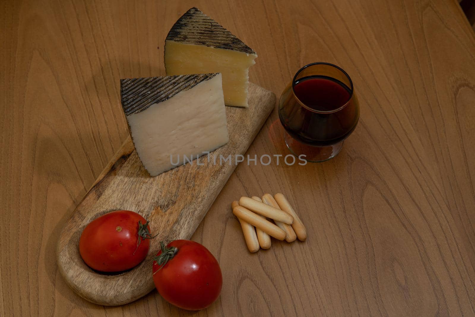 Cheese wedge with tomato, bread sticks and red wine