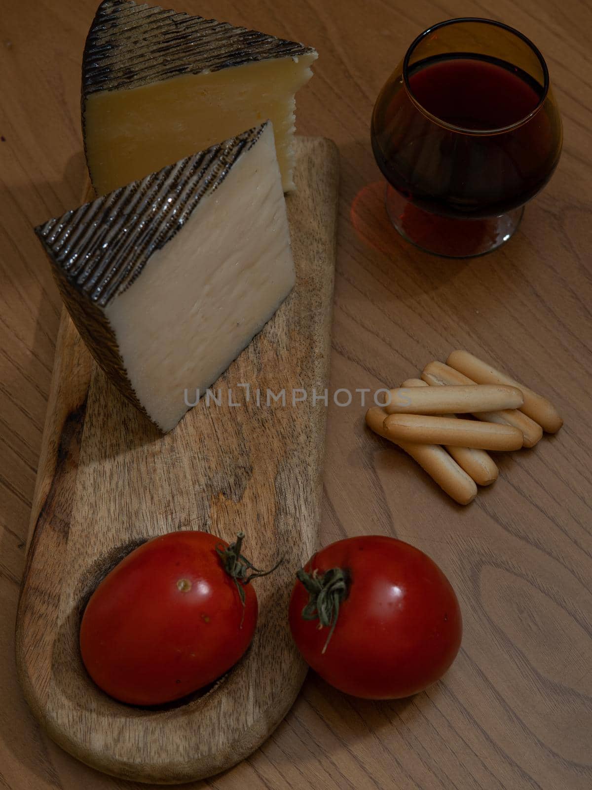 Cheese wedge with tomato and breadsticks on wooden board