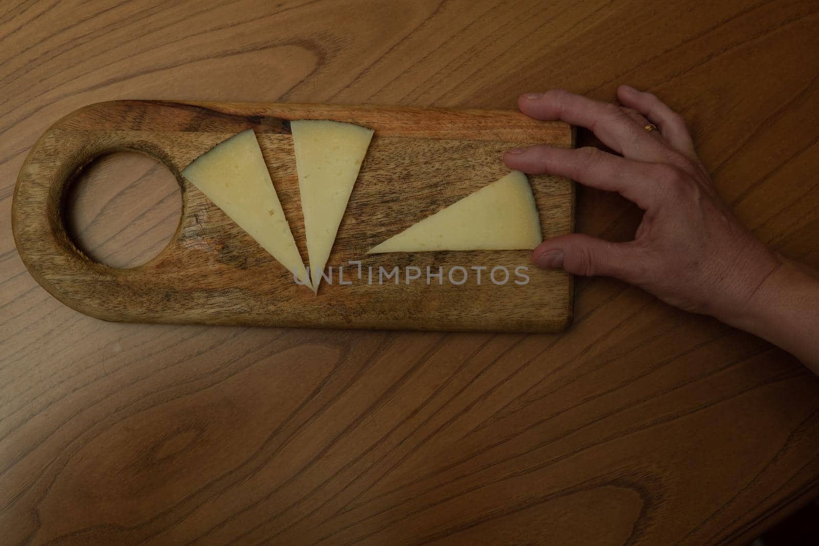 Hand holding triangle of cheese on wooden background by xavier_photo