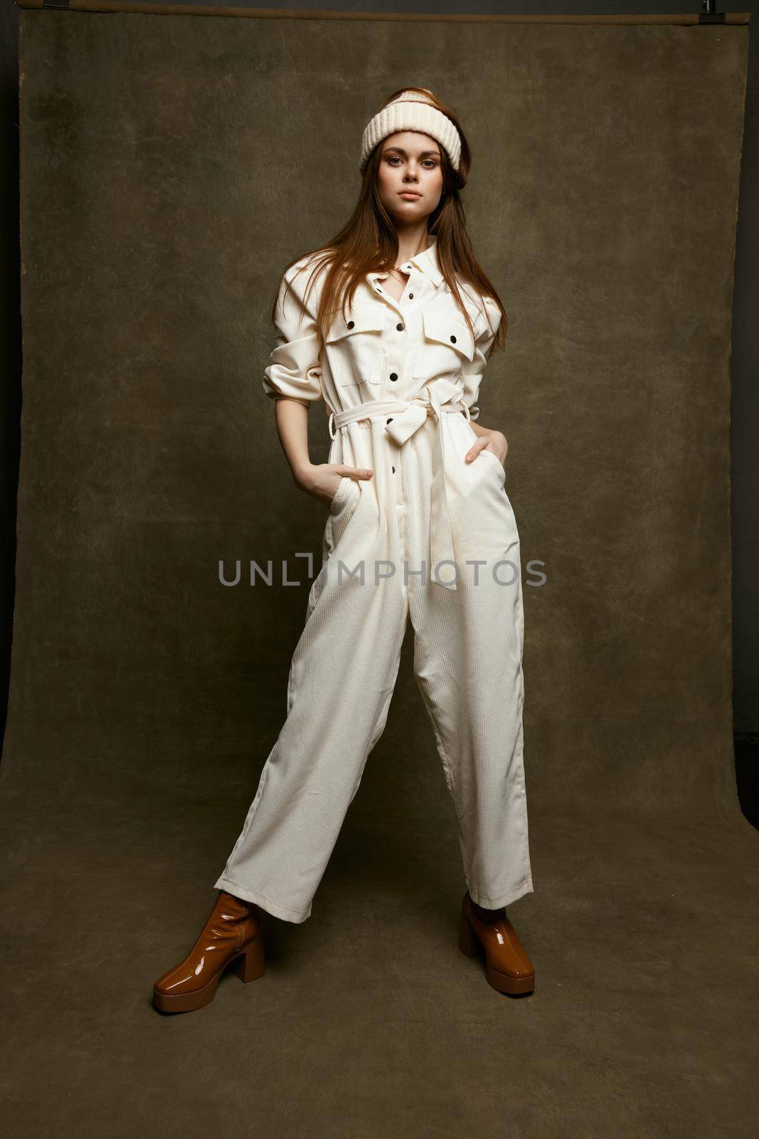 fashionable woman in a white jumpsuit holds hands in pockets and a hat on her head brown shoes by SHOTPRIME