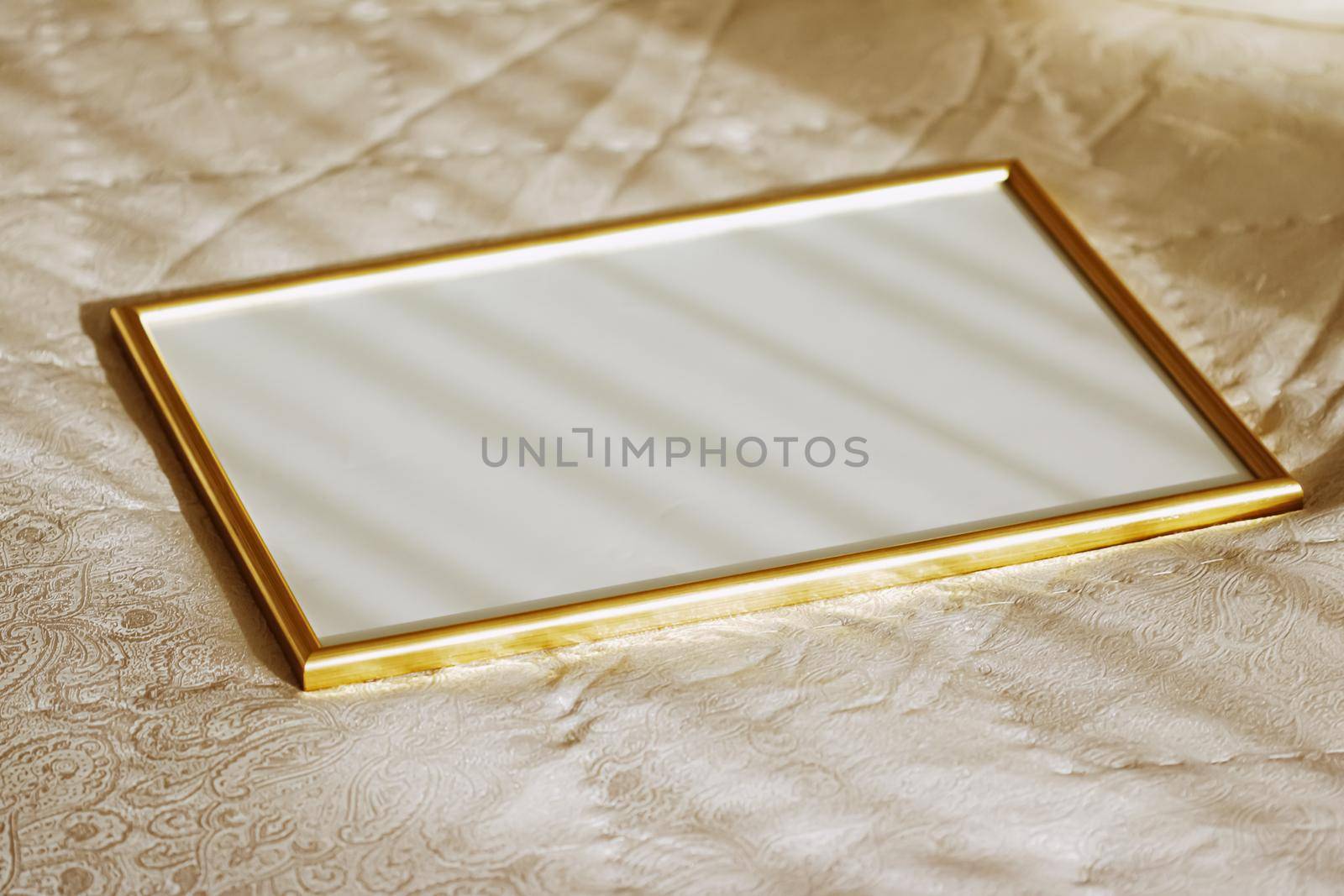 Golden frame for art, poster or photo on bed at sunset, home decor concept