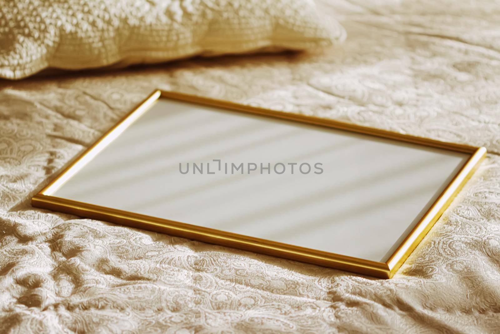 Golden frame for art, poster or photo on bed at sunset, home decor concept
