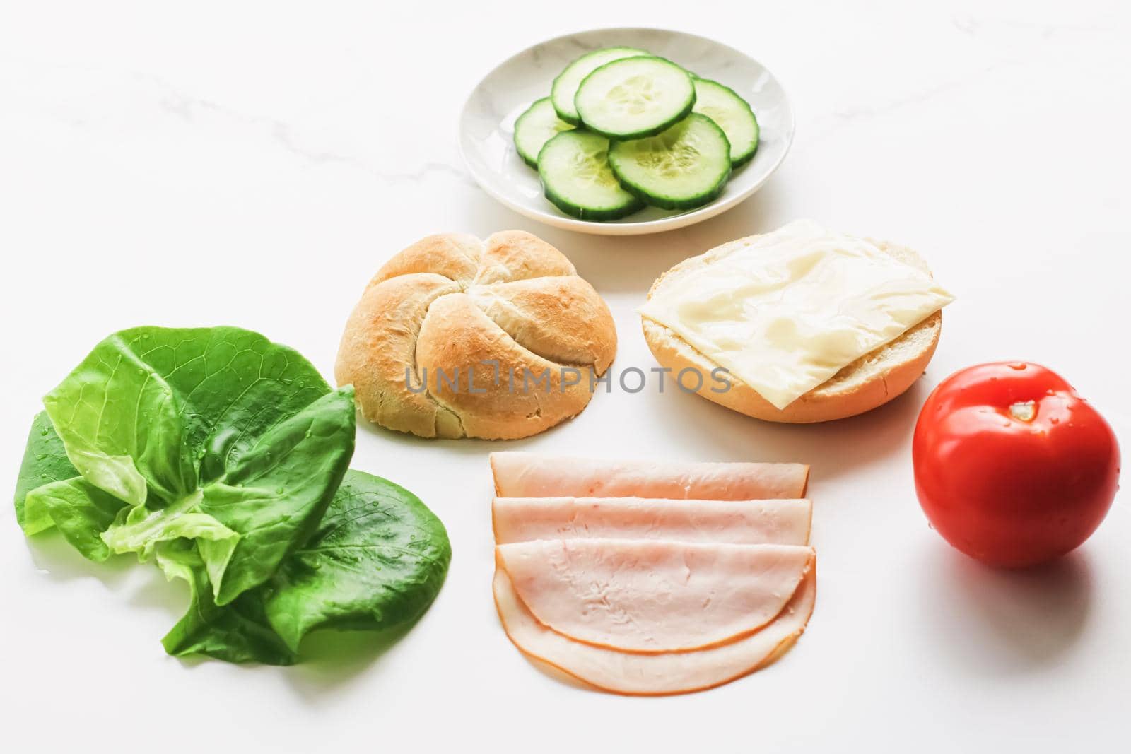 Food products and ingredients for making sandwich. Ham, cheese, burger bun, lettuce, cucumber and tomato as recipe flatlay on marble kitchen table background