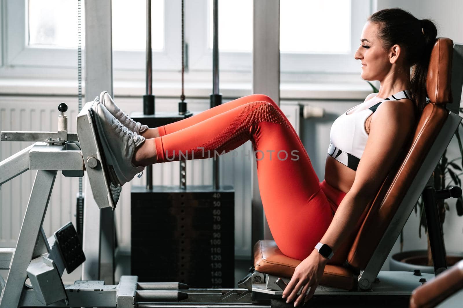 Exercising legs on machine in gym, female fitness instructor.