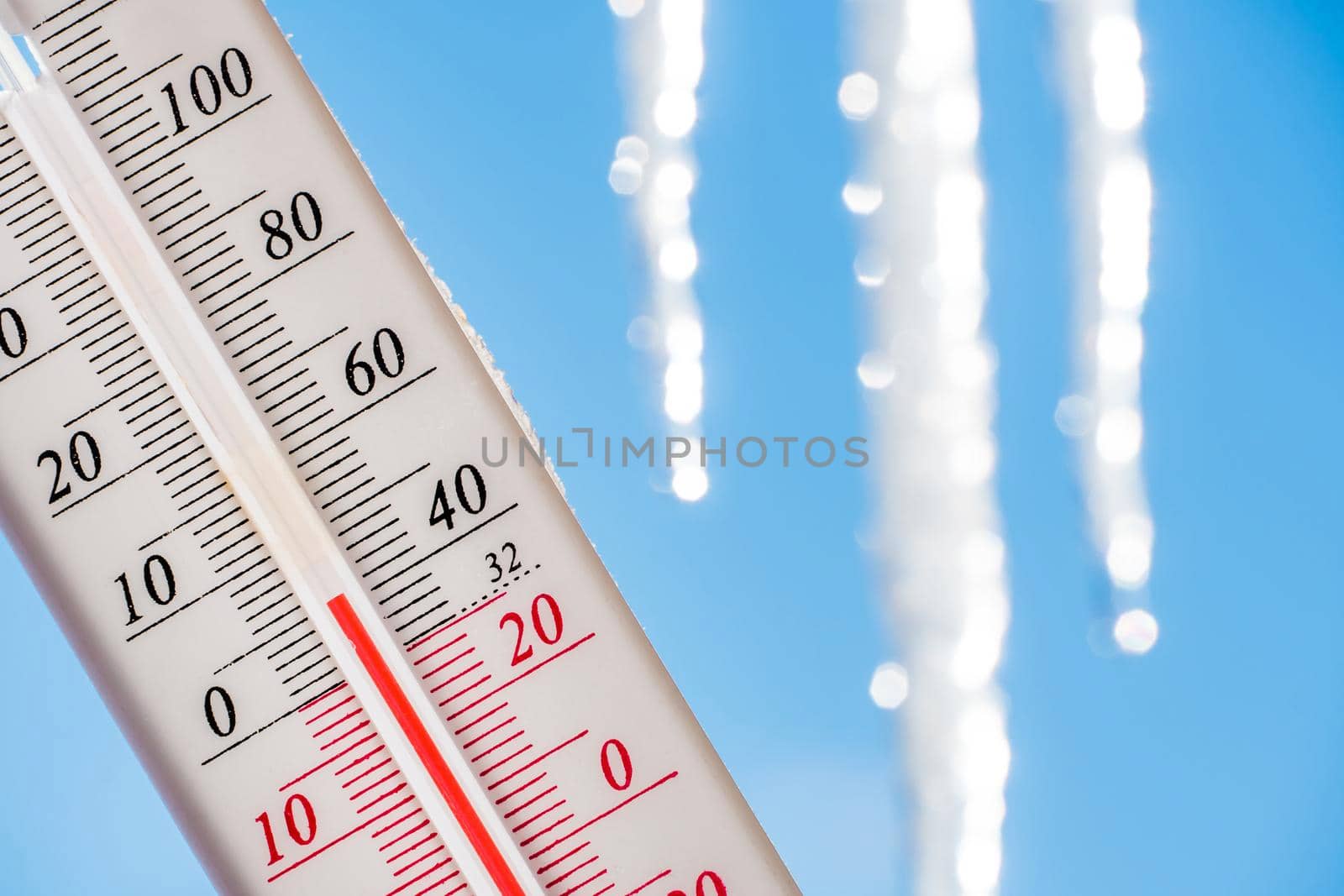 In the spring, the thermometer is on the background of melting icicles and shows a negative temperature.Meteorological conditions,climate change, and global warming.Cold season.