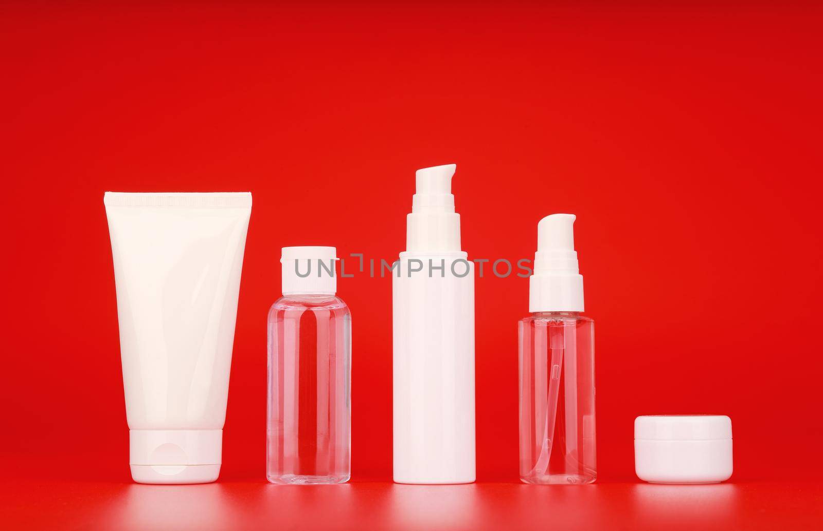 Wide set of cosmetic products for skin care against red background. Concept of daily skin cleaning, exfoliating, moisturizing and anti aging treatment