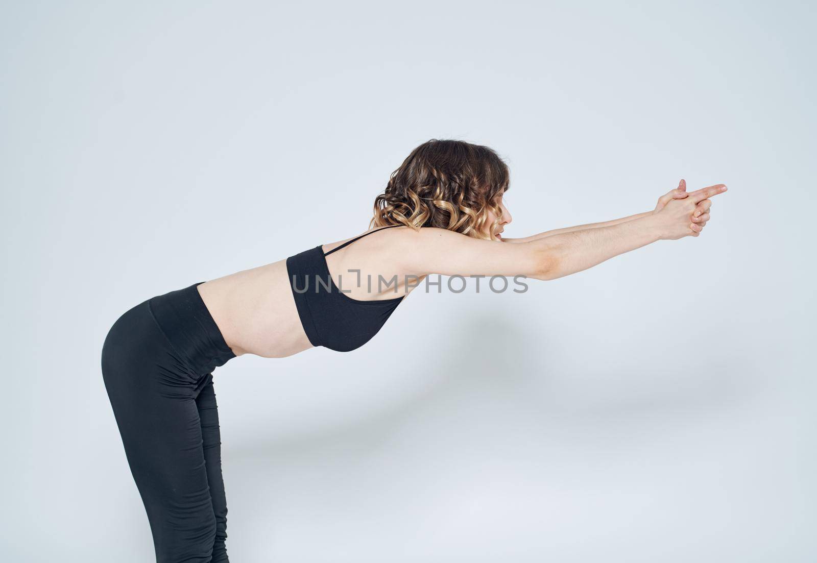 A sportive woman in leggings and a short T-shirt is gesturing with her hands on a light background. High quality photo