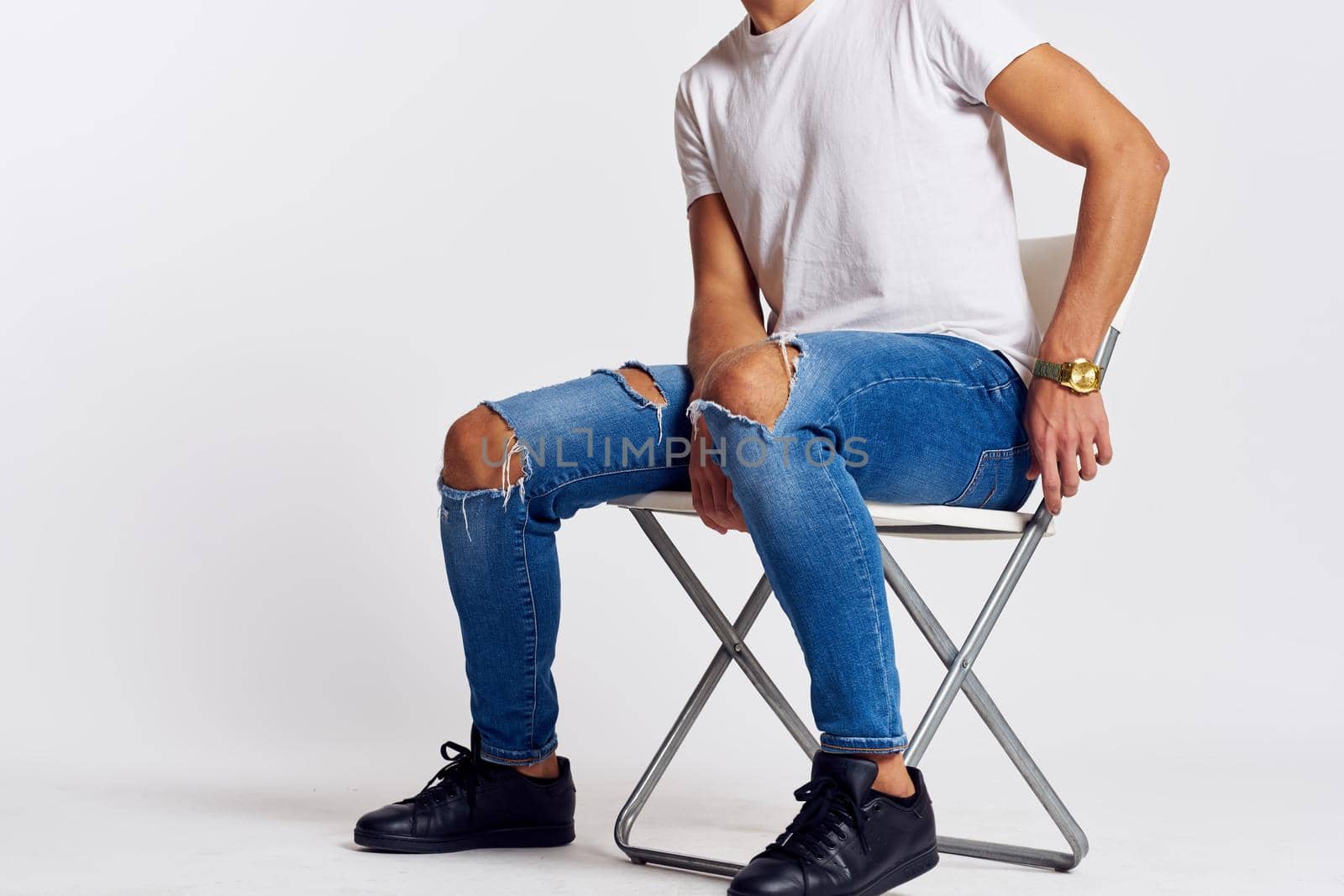 a man in jeans and a t-shirt sits on a chair on a light background side view. High quality photo