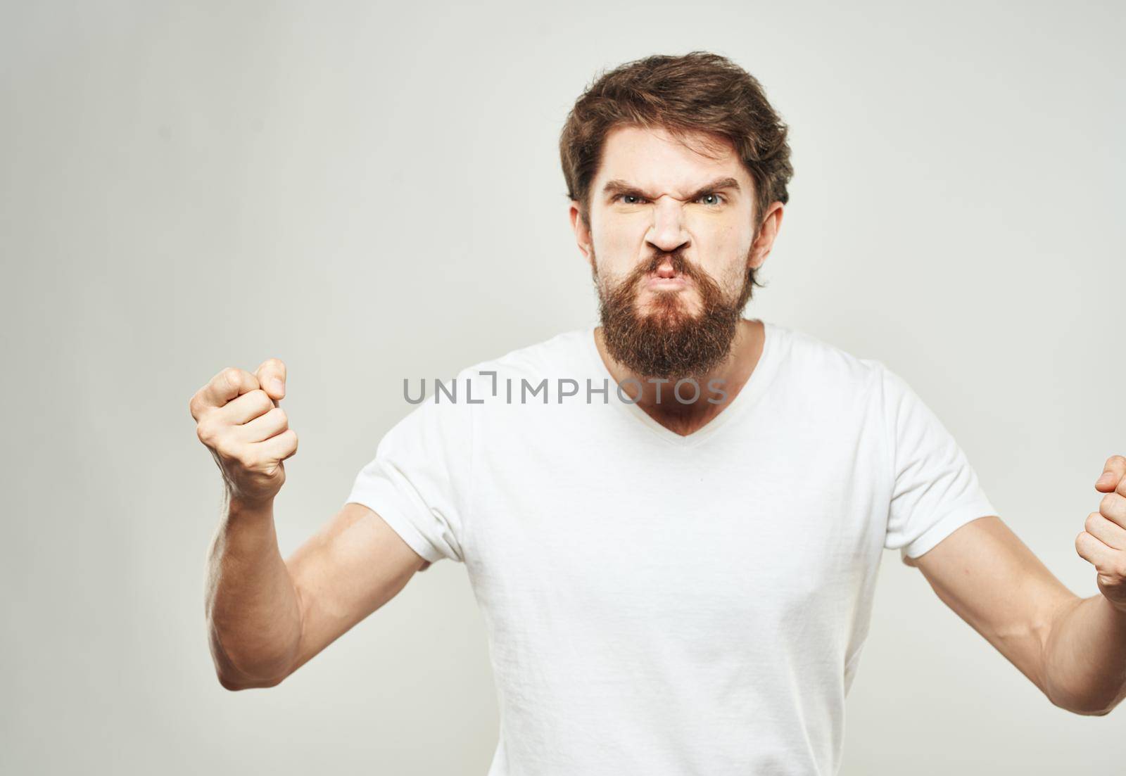 Indignant man in a white T-shirt gesturing with his hands on a light background cropped view. High quality photo