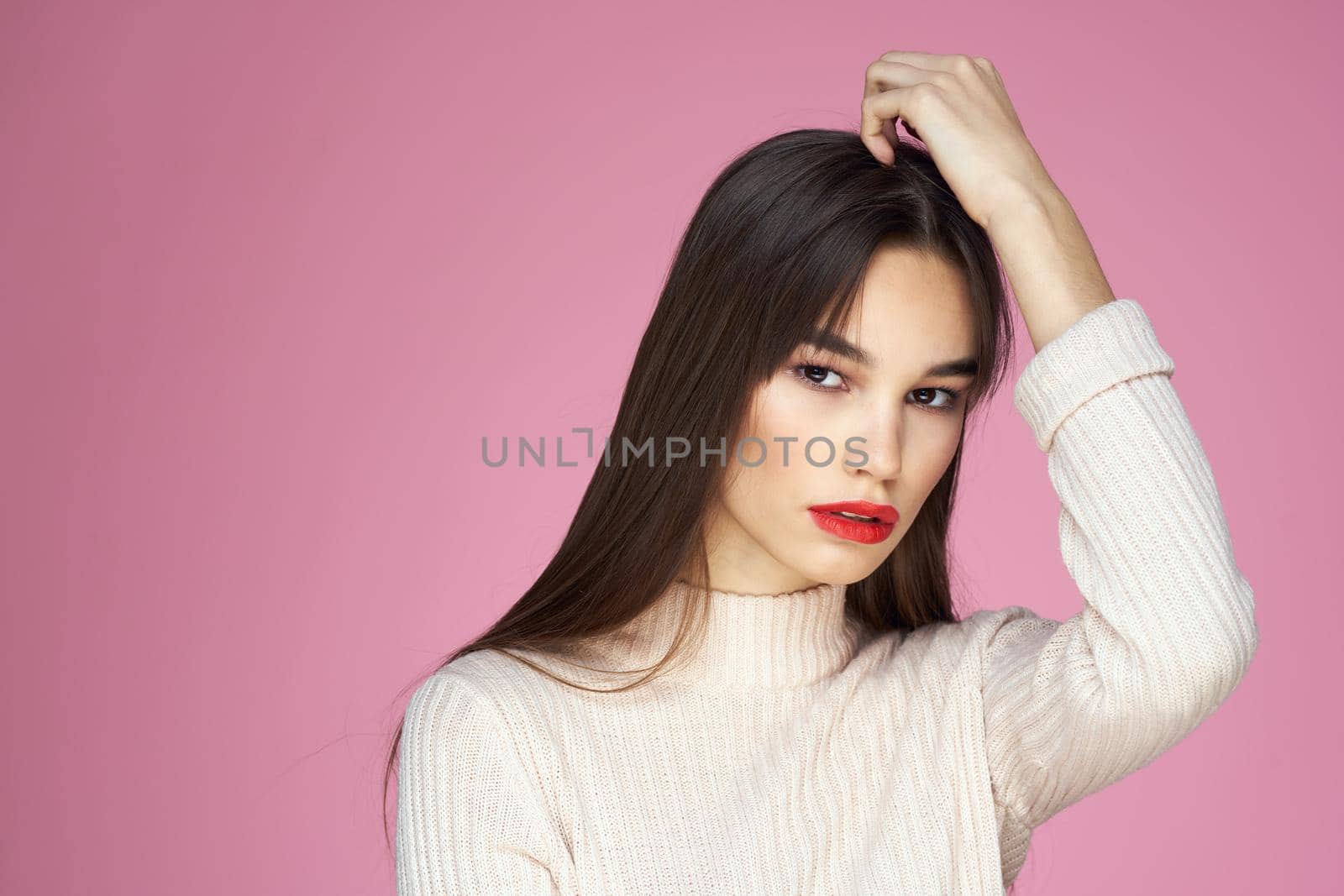 Pretty brunette in a white sweater red lips attractive look pink background. High quality photo