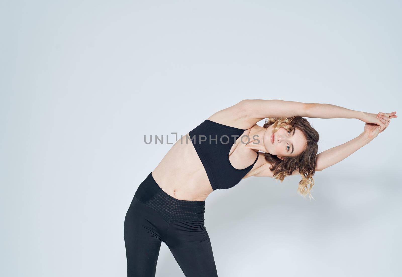 A woman in leggings has joined her hands above her head and is doing the exercises, bends to the side. High quality photo