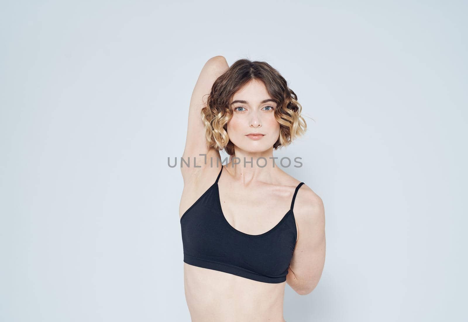 A strange woman in a short T-shirt has joined her hands behind her back on a light background by SHOTPRIME