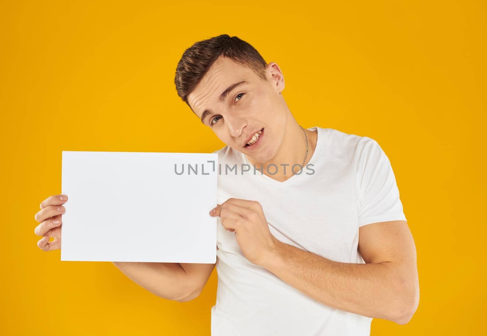 The guy with a sheet of paper on a yellow background tilted his head to the side cropped view. High quality photo