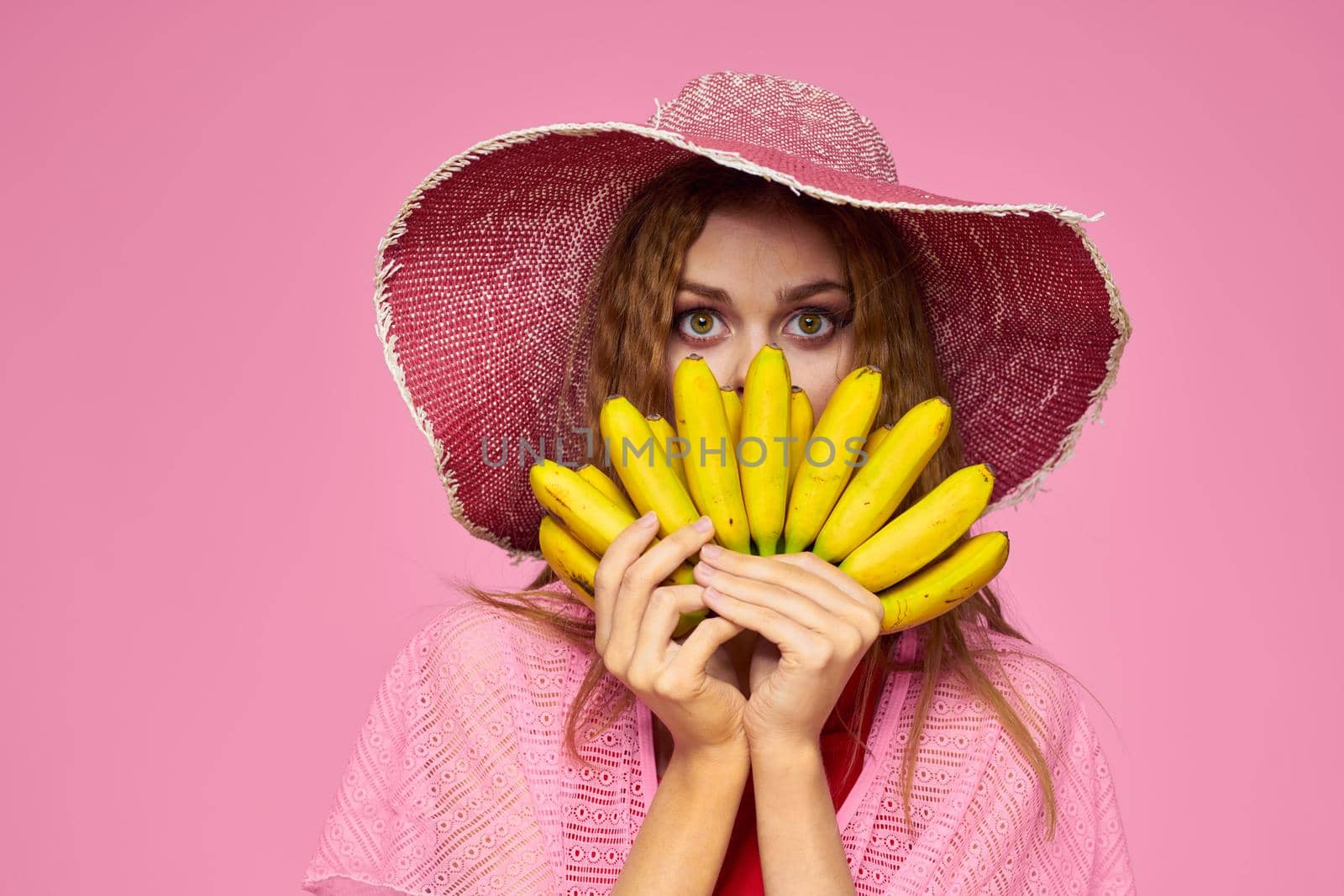 Woman with bananas in hands in hat exotic fruits lifestyle pink background. High quality photo